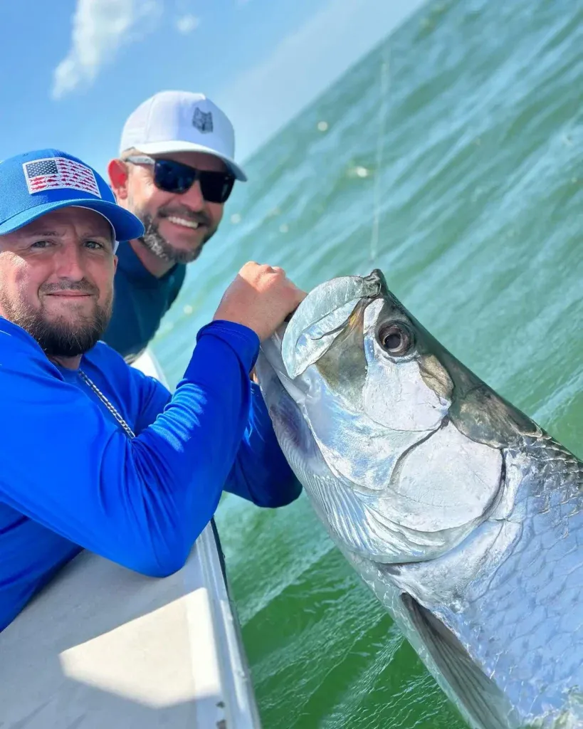 Two anglers holding a trophy tarpon beside a charter boat in Sarasota, Florida.